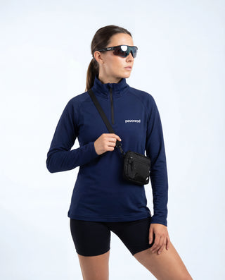 Haut technique demi-zip Pavenrod bleu marine Made in France porté par une femme avec lunettes et sacoche bandoulière, tenue outdoor, fond blanc.