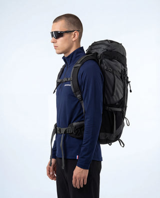 Haut technique demi-zip Pavenrod bleu marine Made in France, vue de profil, porté par un homme avec sac à dos de randonnée et lunettes, fond blanc.
