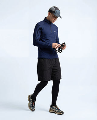 Haut technique demi-zip Pavenrod bleu marine Made in France porté par un homme, short de trail et collant, tenant une lampe frontale, fond blanc.