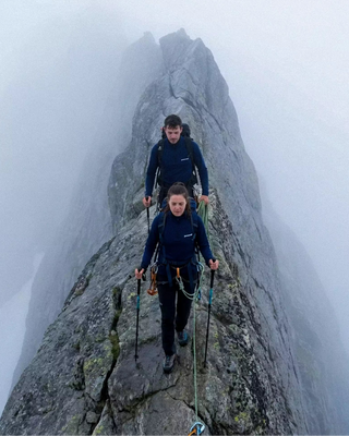 Deux randonneurs en hauts techniques zippés Pavenrod sur une arête étroite dans le brouillard, progression encordée en montagne.