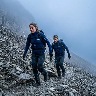 Femme et homme en hauts techniques zippés Pavenrod, marche en terrain pierreux sous conditions froides avec neige, sacs à dos en montagne.