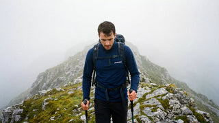Randonneur sur une crête dans le brouillard, haut technique zippé Pavenrod et bâtons de marche, ambiance humide en montagne.