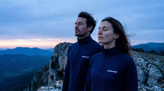 Homme et femme portant un haut technique manches longues zippé Pavenrod bleu nuit, sur une arête au crépuscule en montagne.