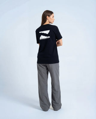 Femme portant t-shirt Pavenrod noir coton bio fabriqué en France, vue dos trois-quarts, graphisme au dos, photo studio fond clair.