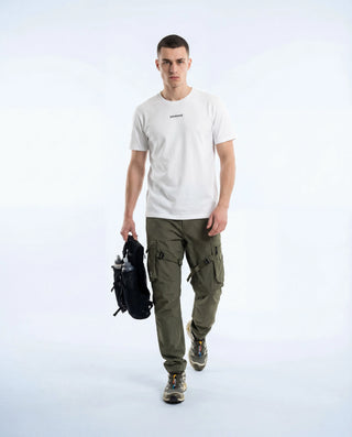 Homme portant t-shirt Pavenrod blanc en coton bio fabriqué en France, vue face en marche avec sac, ambiance randonnée, fond studio clair.